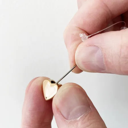 Gold heart-shaped ashes pendant being held between fingers against a white background
