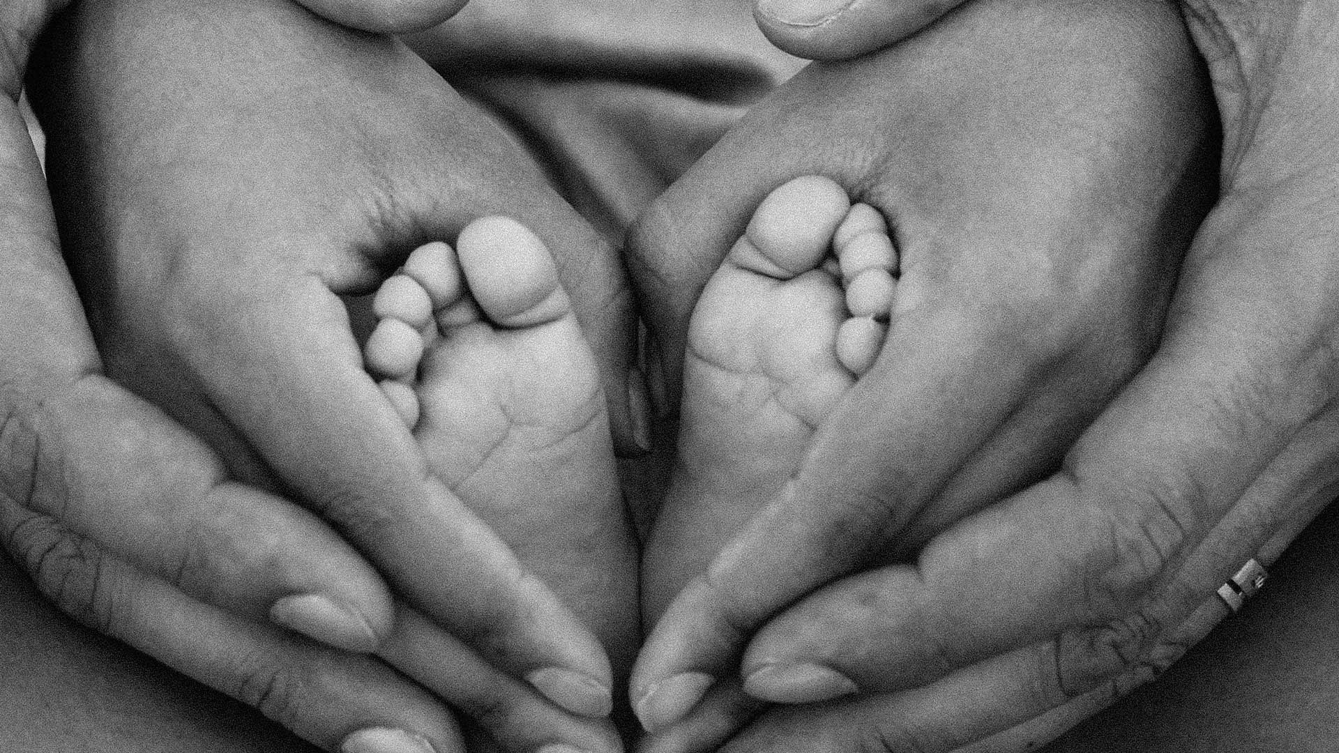 Two adult hands holding a baby's feet in a heart shape.